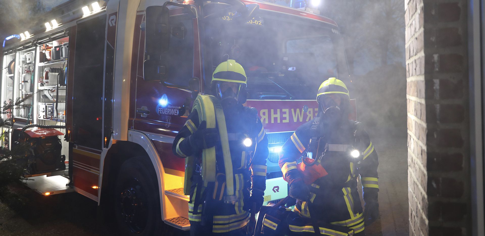 2 Feuerwehrmänner im Einsatz vor einem Feuerwehrwagen